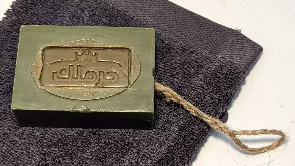 Authentische Aleppo-Seife mit Juteschnur auf einem dunklen Frotteetuch.
