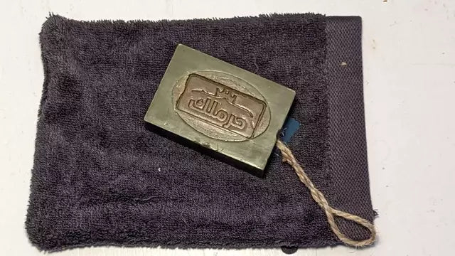Handgemachte Aleppo-Naturseife mit praktischer Aufhängeschlaufe auf einem weichen Handtuch.