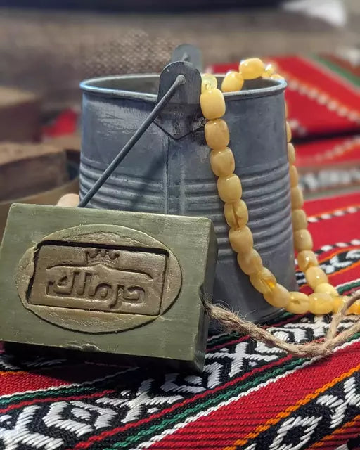 Aleppo-Seife vor dekorativem Hintergrund mit traditionellem Seifeneimer und Kette.