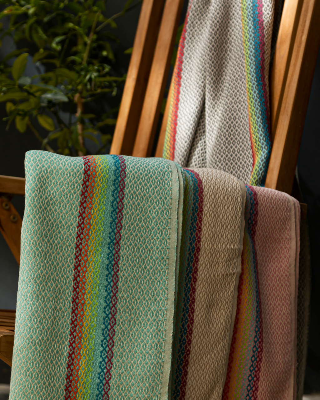 Gefaltetes rosa Samimi Hamamtuch mit Rainbow-Design drapiert über einem Holzstuhl im Außenbereich.