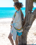 Frau trägt das beige Samimi Bambus-Hamamtuch mit Rainbow-Design als Strandtuch an der Küste.